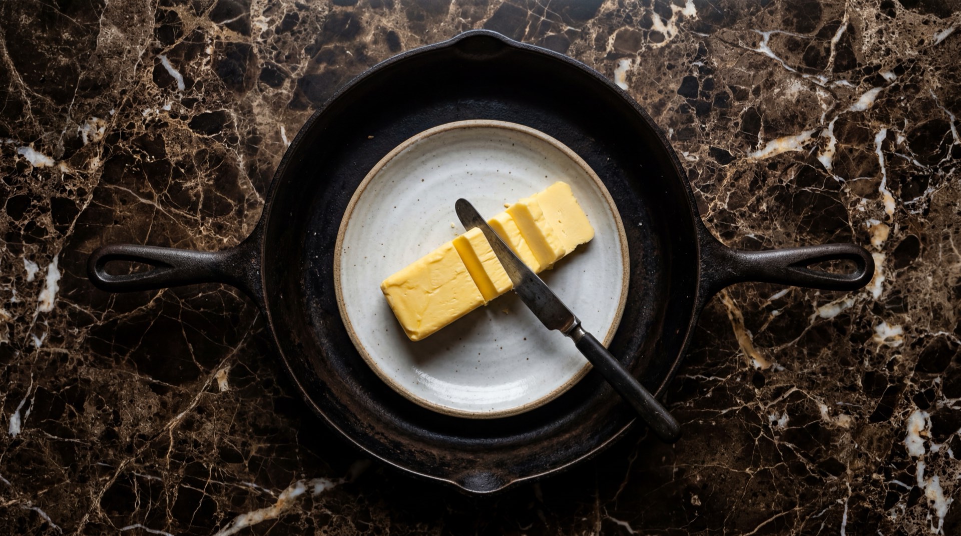 Mantequilla colombiana fresca en barra dorada sobre plato de ceramica negra mate con mesa de marmol negro con vetas doradas