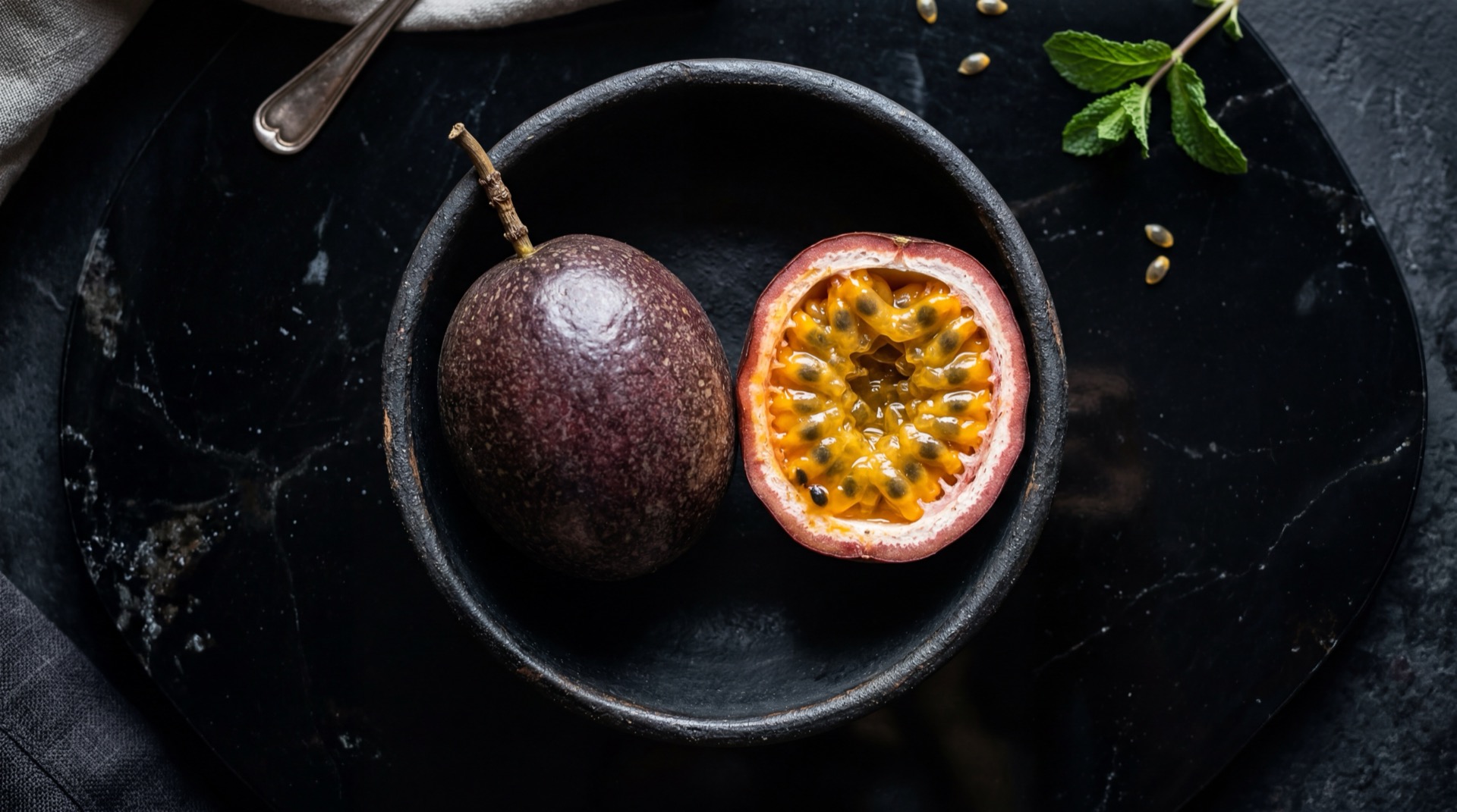 Maracuya amarillo colombiano cortado por la mitad mostrando pulpa anaranjada con semillas negras sobre plato de pizarra oscura