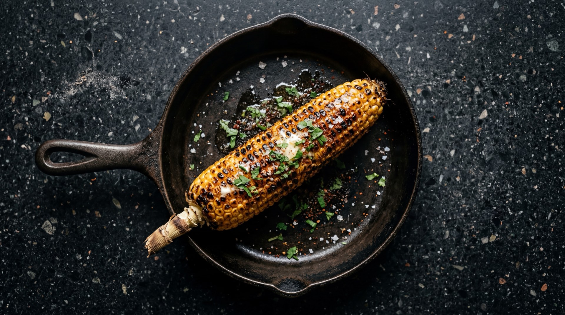 Mazorca colombiana asada a la parrilla con mantequilla derretida y sal gruesa en plato de basalto volcanico sobre mesa de granito negro