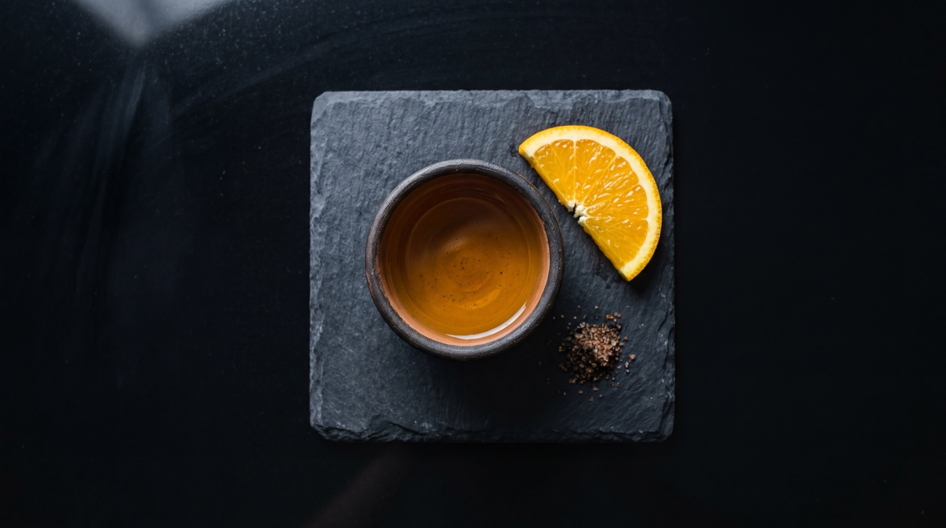 Mezcal mexicano tradicional servido en plato oscuro sobre mesa de marmol negro