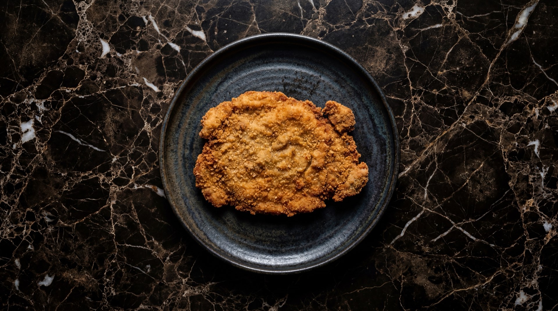 Milanesa argentina de carne de res dorada y crujiente con limon verde sobre tabla de madera oscura