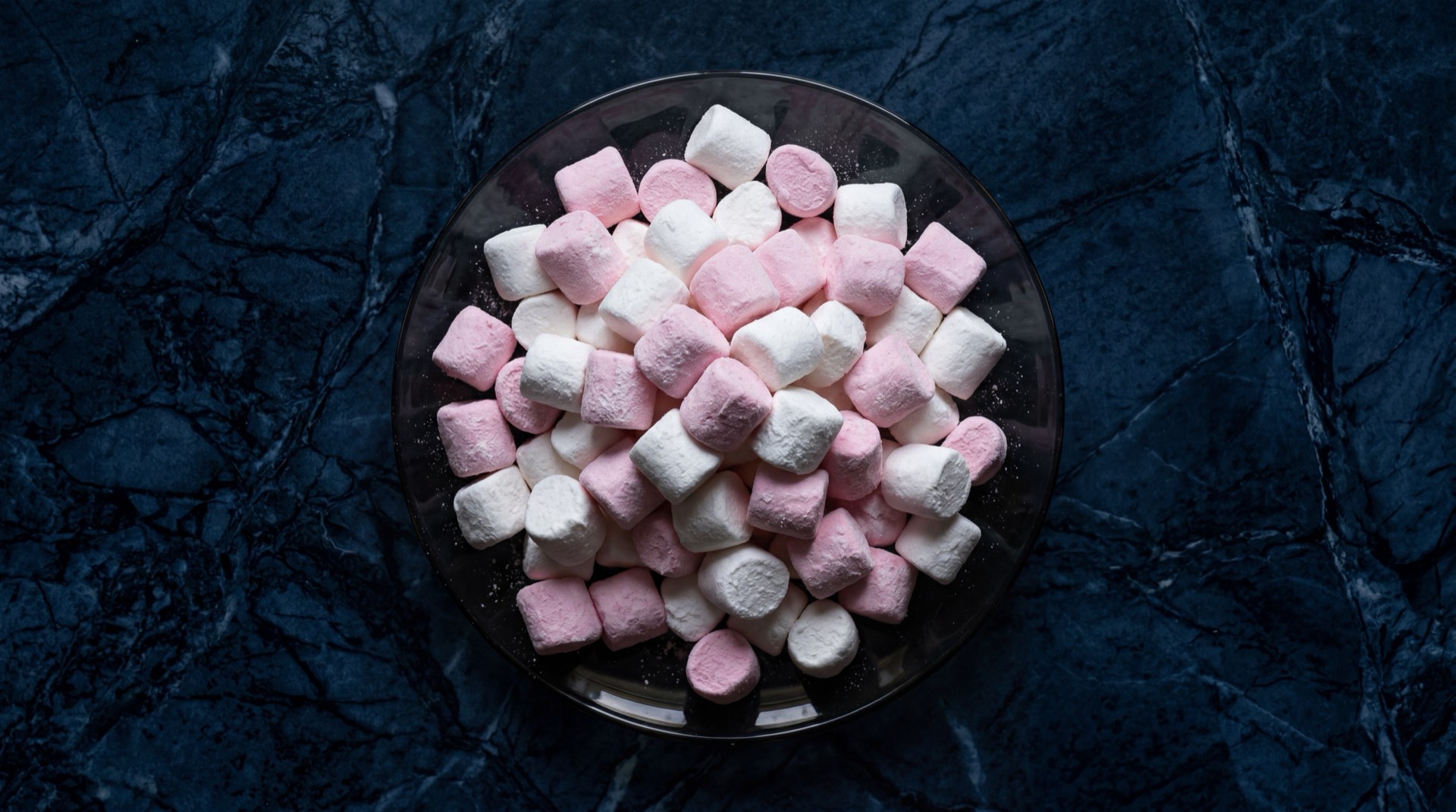 Millows de Colombina, masmelos rosados y blancos sobre plato de ceramica negra sobre mesa de marmol oscuro