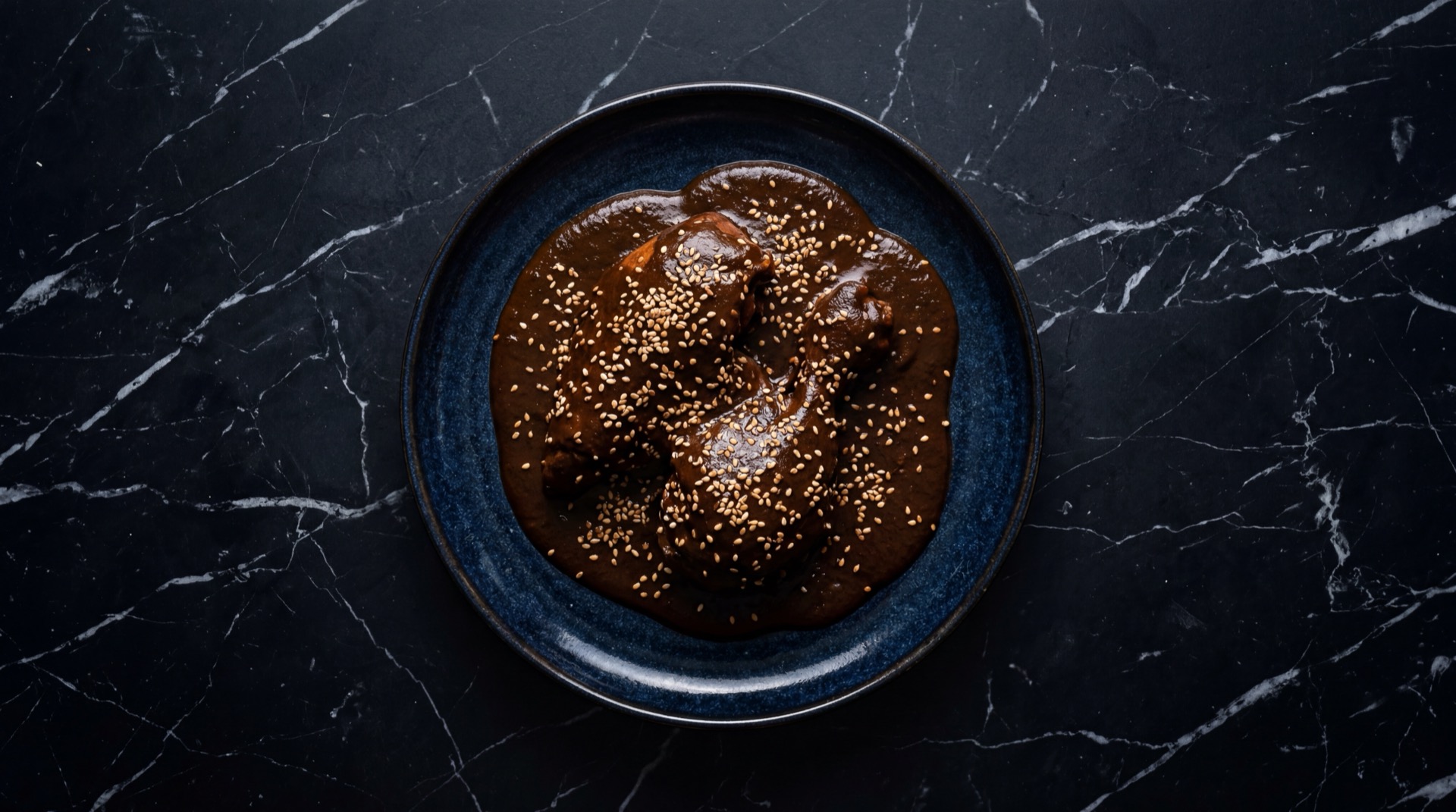 Mole poblano con pieza de pollo banada en salsa oscura espolvoreada con semillas de ajonjoli tostadas en plato de ceramica negra