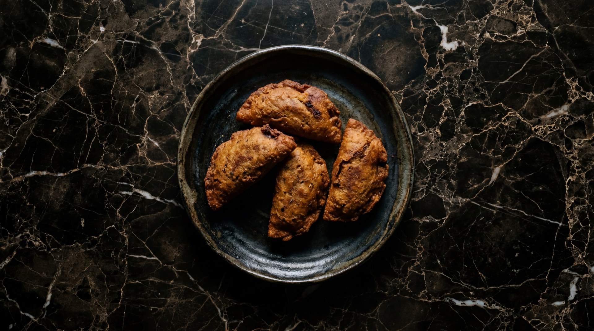 Molotes mexicanos fritos dorados en forma de torpedo sobre bandeja de acero ennegrecido en mesa de concreto carbon