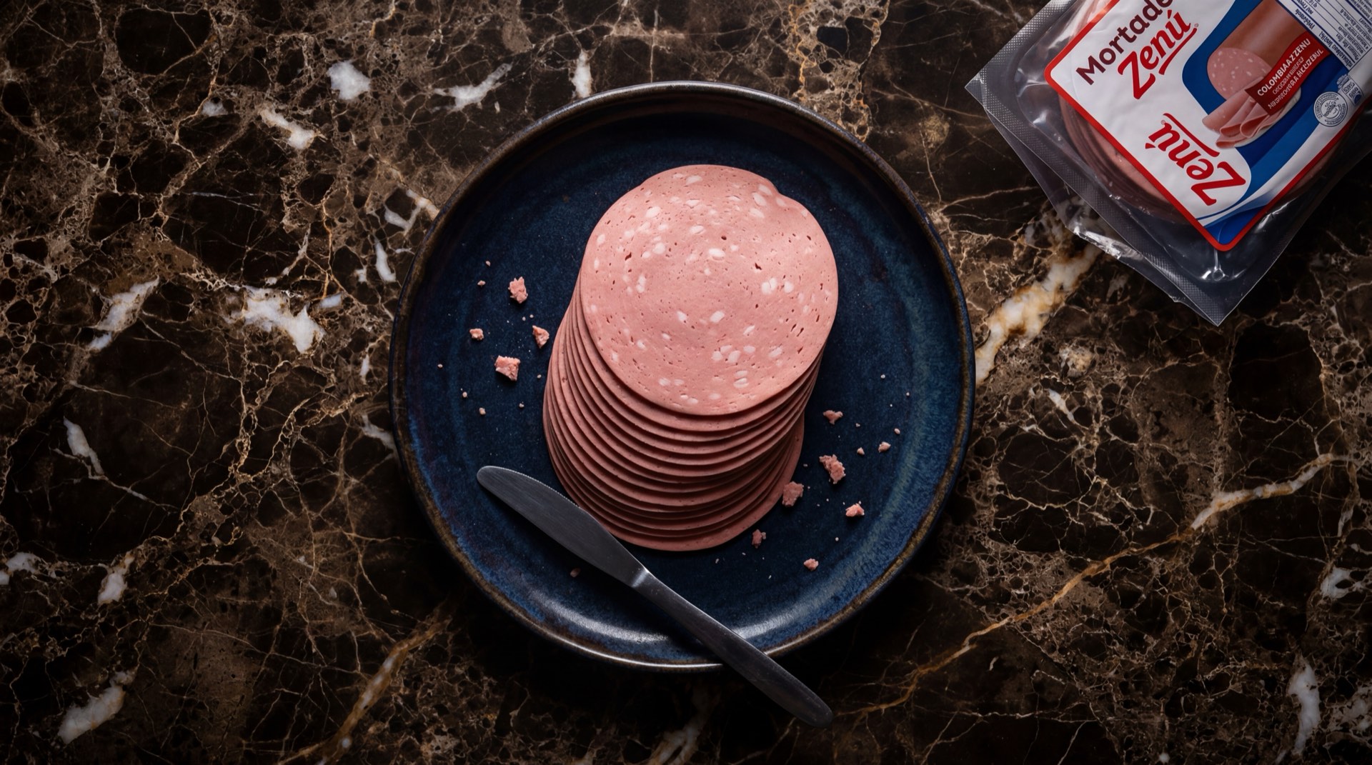 Mortadela Zenu tajada sobre tabla de madera oscura, embutido rosado colombiano de Grupo Nutresa