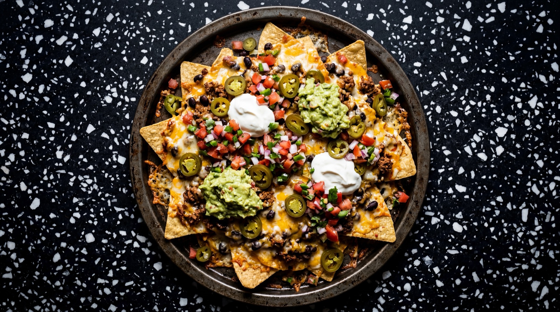 Nachos mexicano tradicional servido en plato oscuro sobre mesa de marmol negro