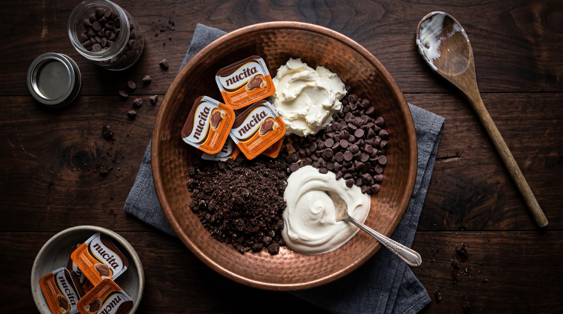 Nucita abierta mostrando la crema bicolor de chocolate oscuro con cacao y crema clara de vainilla con avellana molida, junto a cacao en polvo puro y avellanas enteras