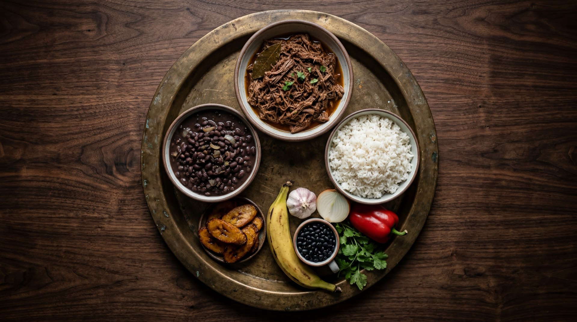 Ingredientes del pabellon criollo venezolano: falda de res cruda entera, caraotas negras secas en recipiente, arroz blanco de grano largo sin cocinar, platanos maduros enteros, cebolla blanca grande, dientes de ajo fresco, ajies dulces venezolanos, pimenton rojo grande y comino molido