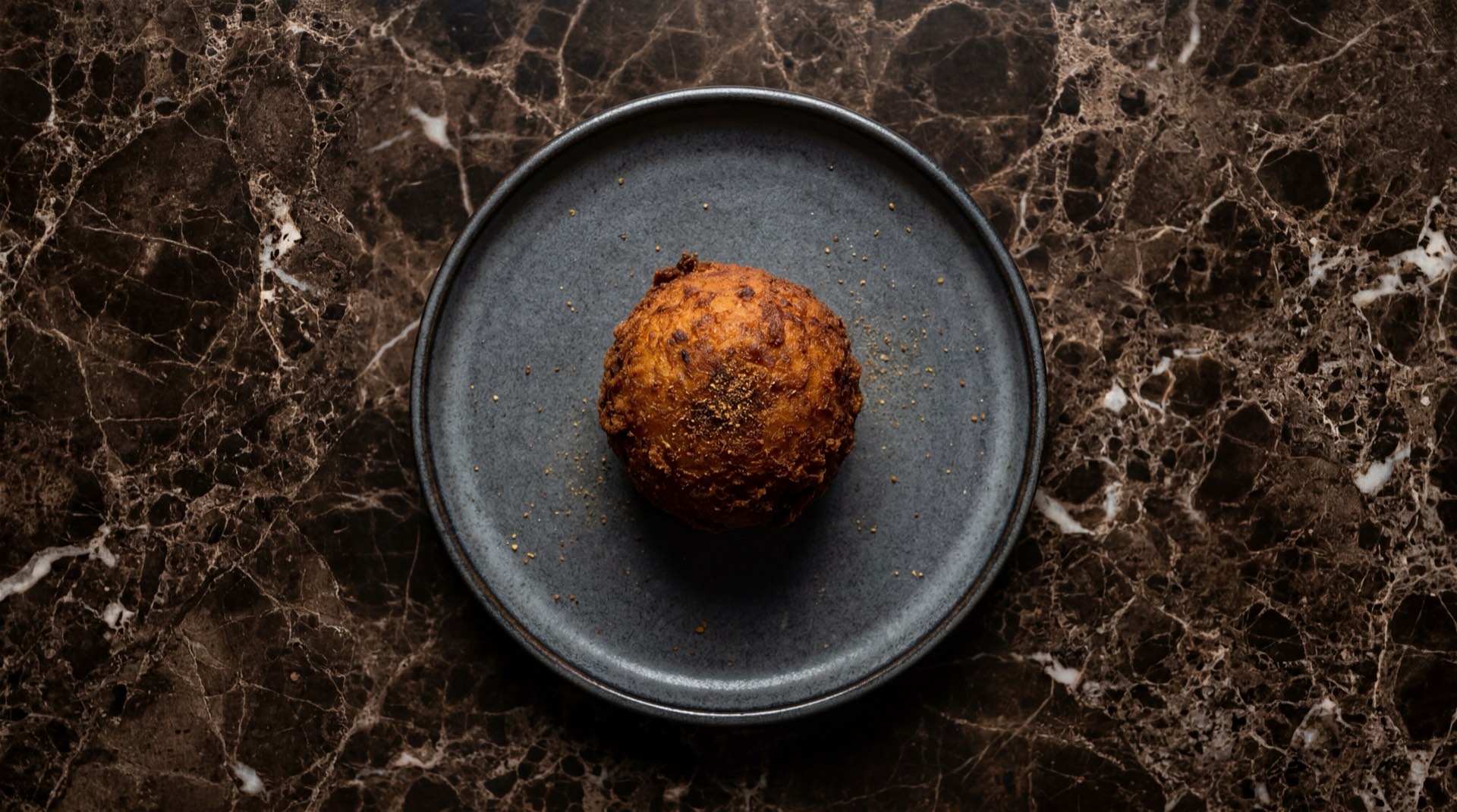 Papa rellena peruana frita dorada cortada por la mitad mostrando relleno de carne molida de res con aceituna negra de botija y huevo duro sobre plato de piedra obsidiana en mesa de marmol negro con vetas blancas