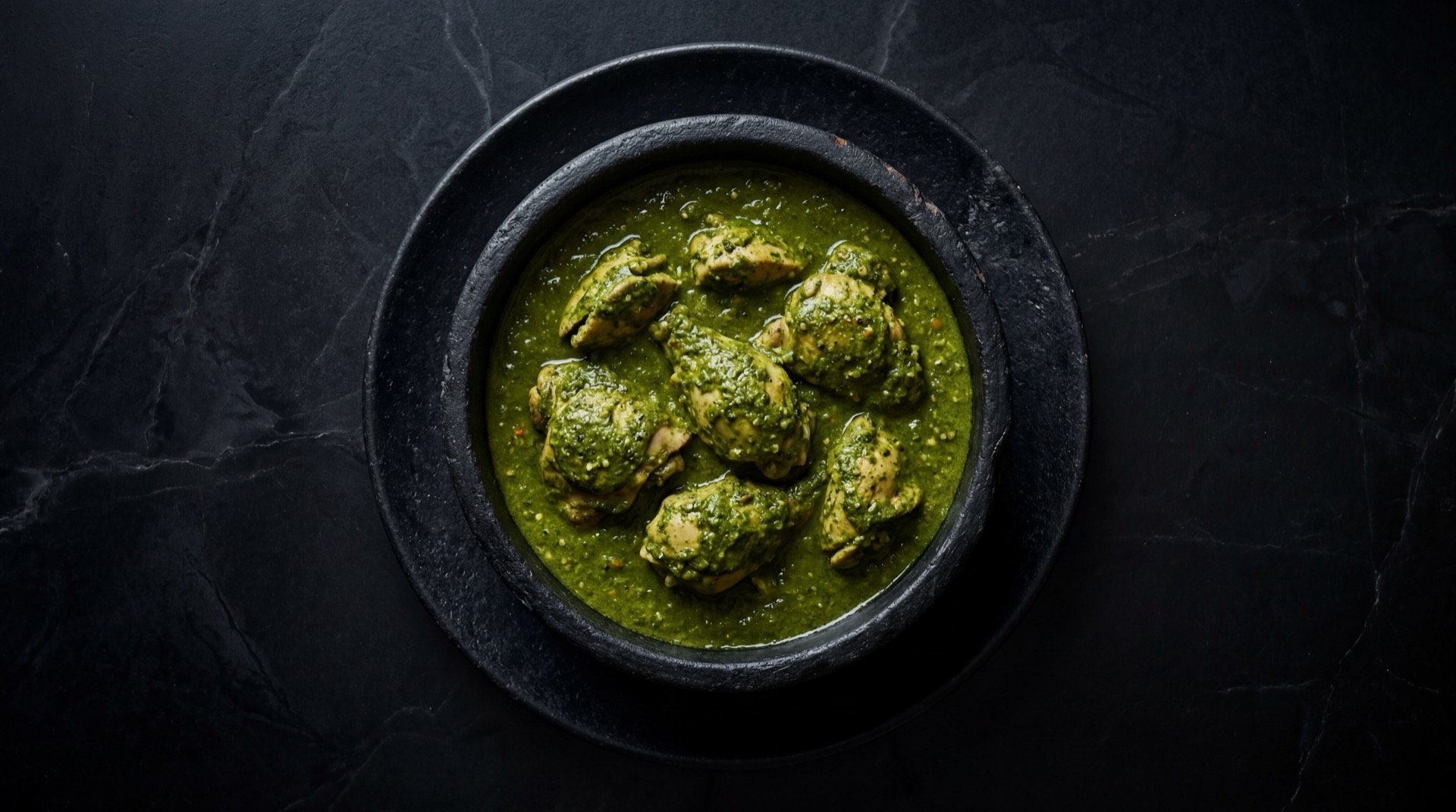 Pipian Verde mexicano tradicional servido en plato oscuro sobre mesa de marmol negro