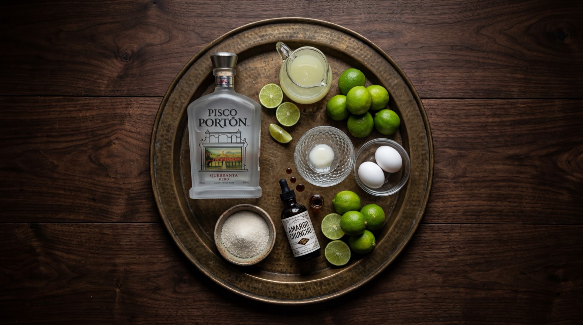 Ingredientes del pisco sour peruano: botella de pisco quebranta peruano, limones verdes peruanos cortados, jarabe de goma en botella de vidrio, huevo fresco con clara separada, amargo de angostura y hielo