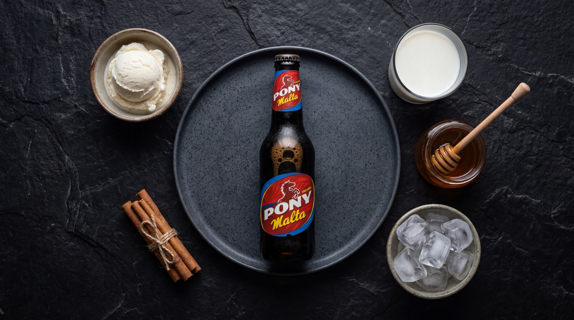 Pony Malta servida en vaso de vidrio mostrando el liquido marron oscuro con espuma cremosa, con granos de cebada malteada tostada y conos de lupulo seco al lado