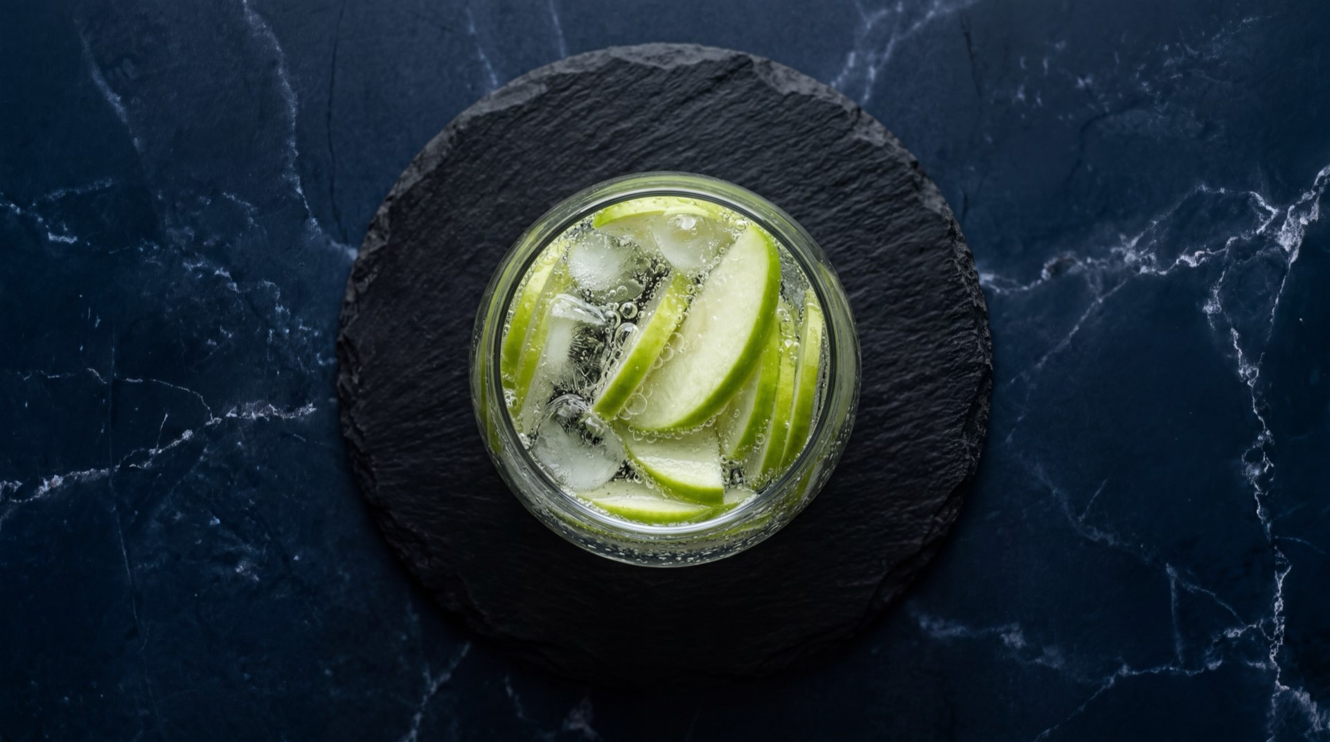 Alternativa saludable a la Postobon Manzana: agua mineral gasificada con rodajas de manzana verde fresca y hielo en vaso de vidrio