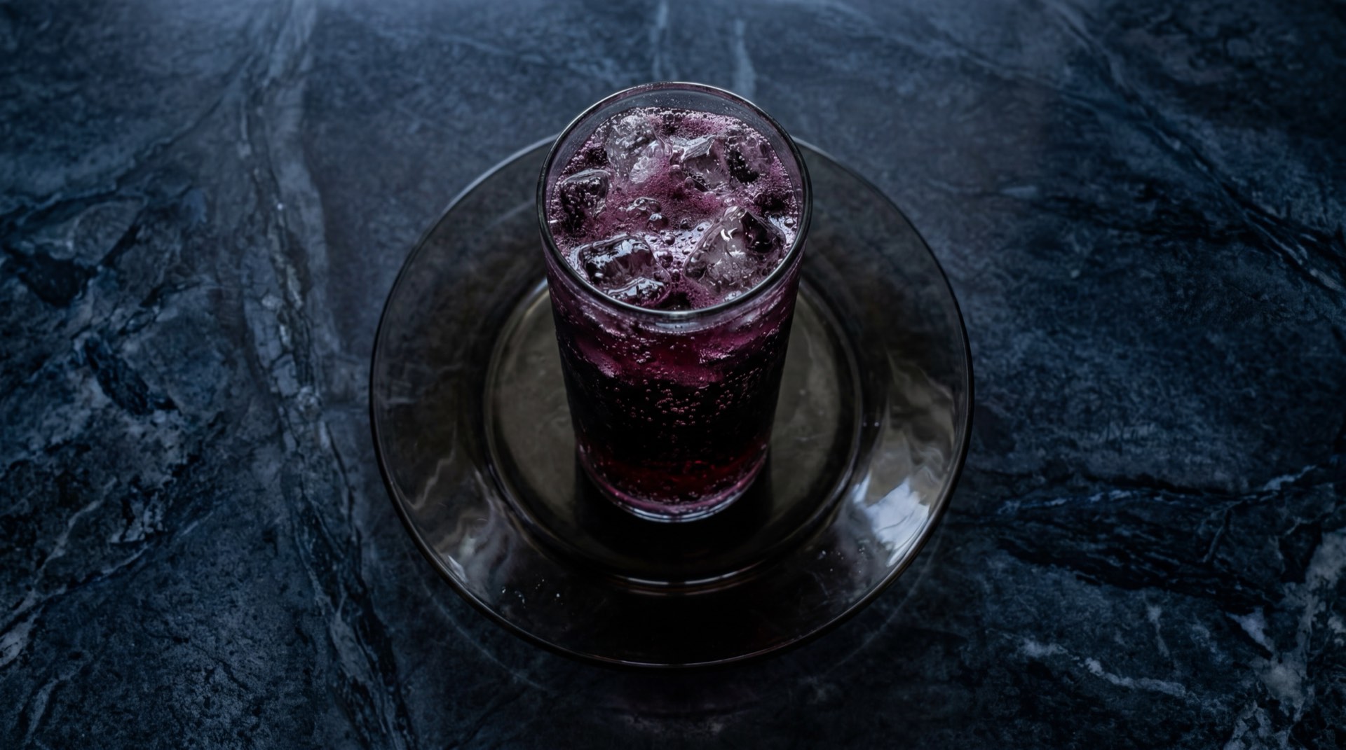 Postobon Uva botella de vidrio con liquido morado gasificado sobre mesa de marmol negro con vetas blancas