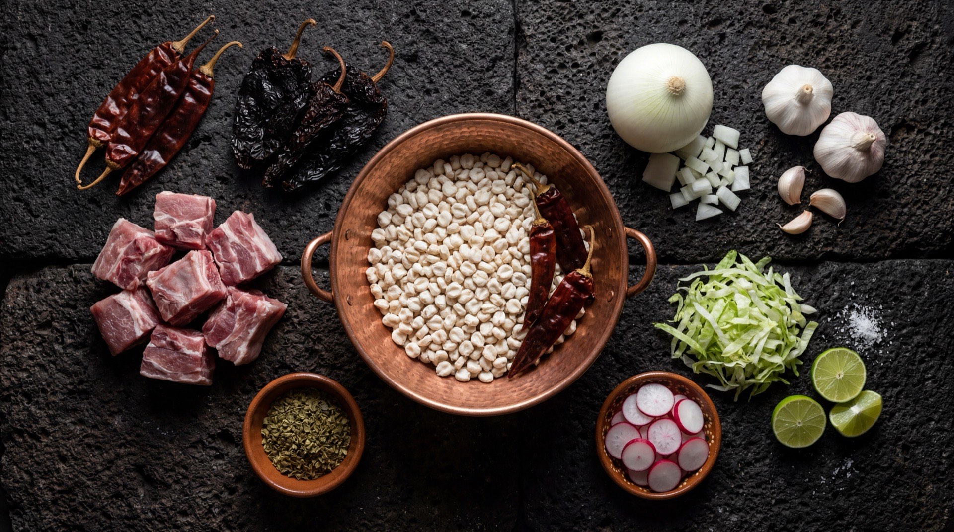 Ingredientes del pozole rojo mexicano: maiz pozolero cacahuazintle seco, chiles guajillo secos desvenados, chiles ancho secos desvenados, carne de cerdo en trozos con hueso, dientes de ajo pelados enteros, cebolla blanca mediana, oregano mexicano seco, rabanos rojos frescos y limones verdes mexicanos