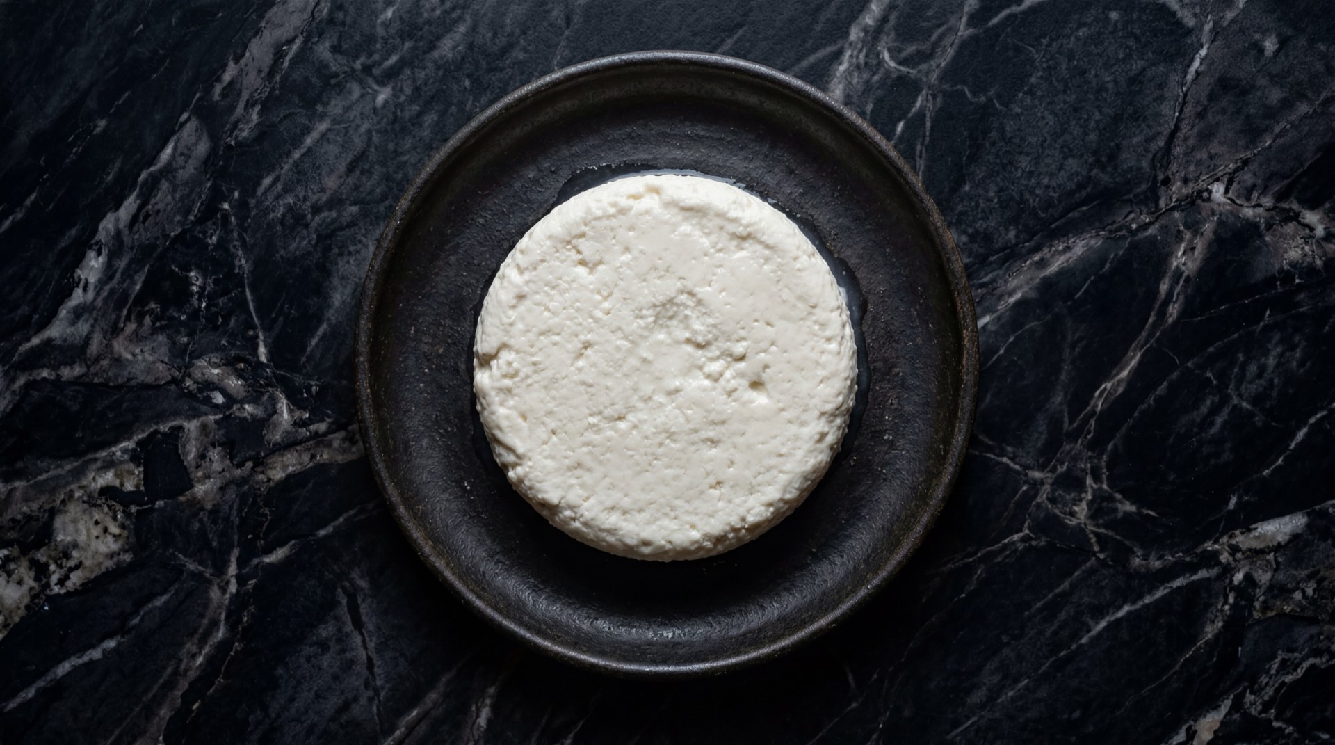 Quesitos antioquenos frescos blancos en forma de bolitas sobre cazuela de terracota oscura en mesa de nogal oscuro