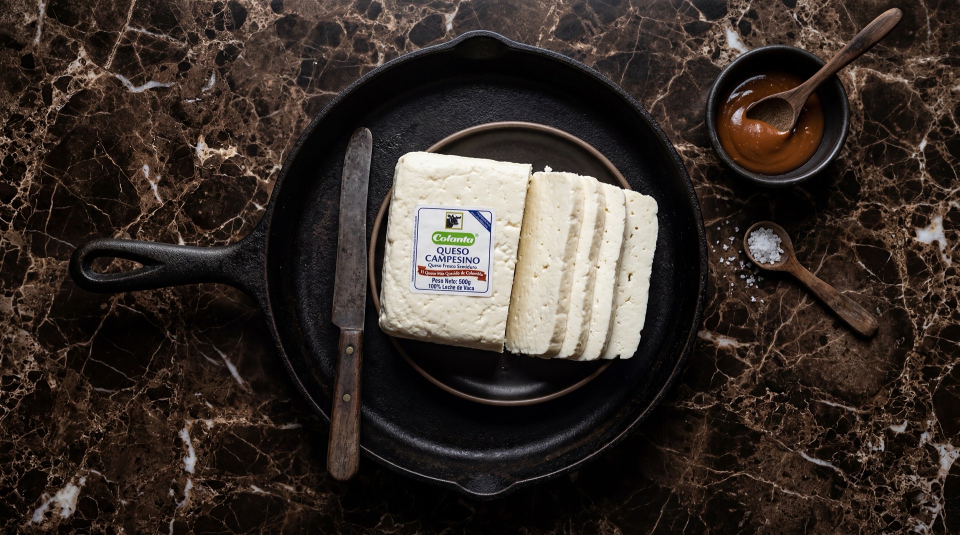 Queso campesino Colanta blanco fresco cortado en tajadas gruesas sobre tabla de madera oscura con fondo de marmol negro
