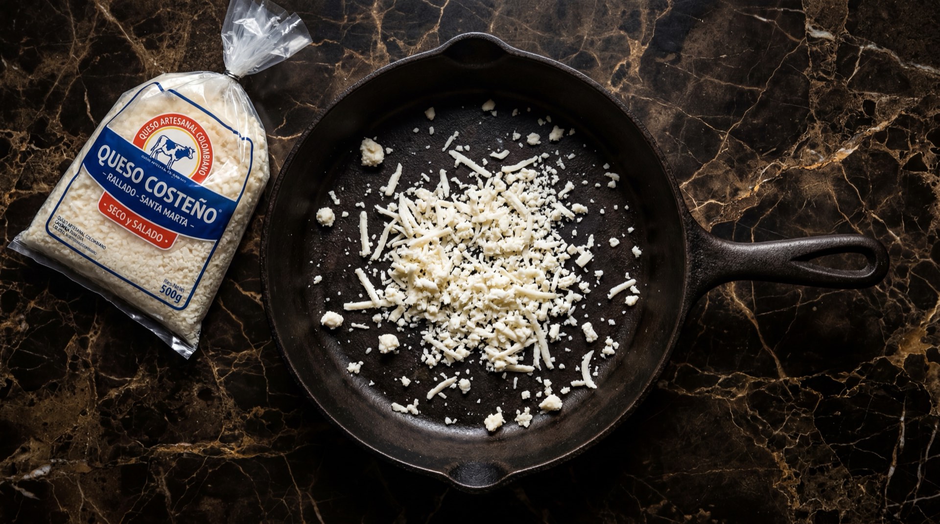 Queso costeno rallado colombiano seco y salado en bolsa sobre plato de ceramica negra mate en mesa de marmol negro con vetas doradas