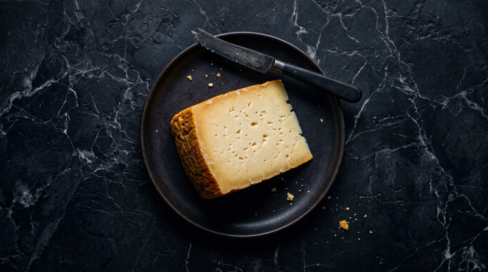 Queso paipa madurado de Boyaca Colombia con corteza natural dorada sobre placa de piedra volcanica en mesa de marmol negro Marquina