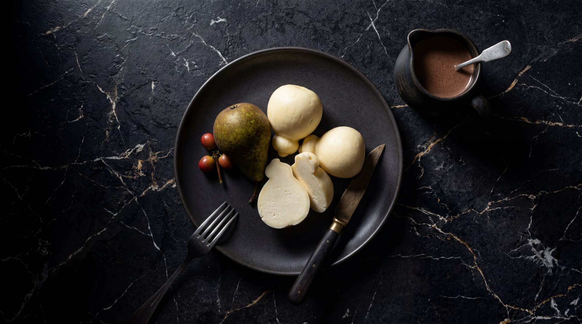 Queso pera colombiano entero con textura lisa y brillante sobre plancha de hierro fundido oscuro en mesa de piedra caliza negra