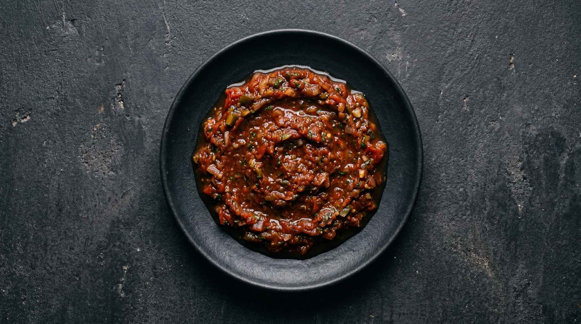Salsa roja mexicana version sin aceite con jitomate asado y chile de arbol en tazoncito de ceramica sobre mesa oscura