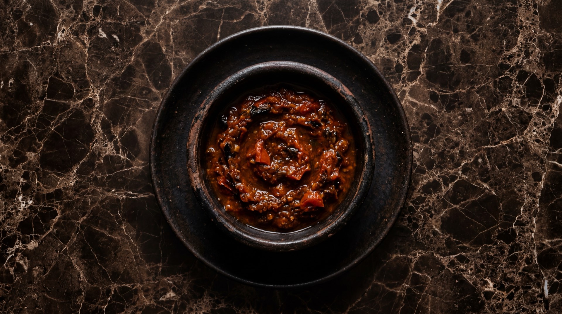 Salsa roja mexicana casera de jitomate asado con chile de arbol en molcajete de piedra volcanica sobre mesa de nogal oscuro