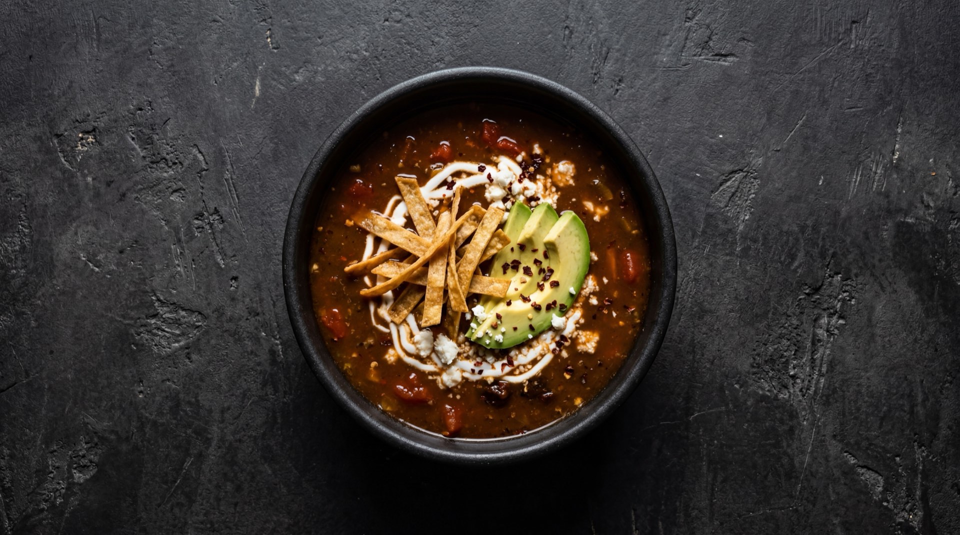 Sopa azteca mexicana version saludable con tiras de tortilla horneadas y cubos de aguacate maduro sin crema en tazon de ceramica