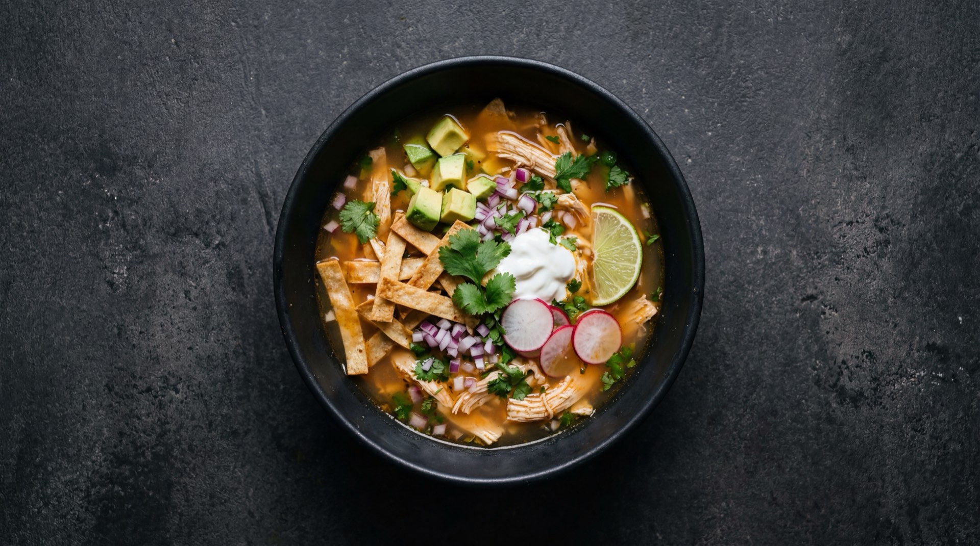 Sopa de tortilla version ligera con tiras de tortilla de maiz horneadas sin freir y menos crema sobre mesa oscura