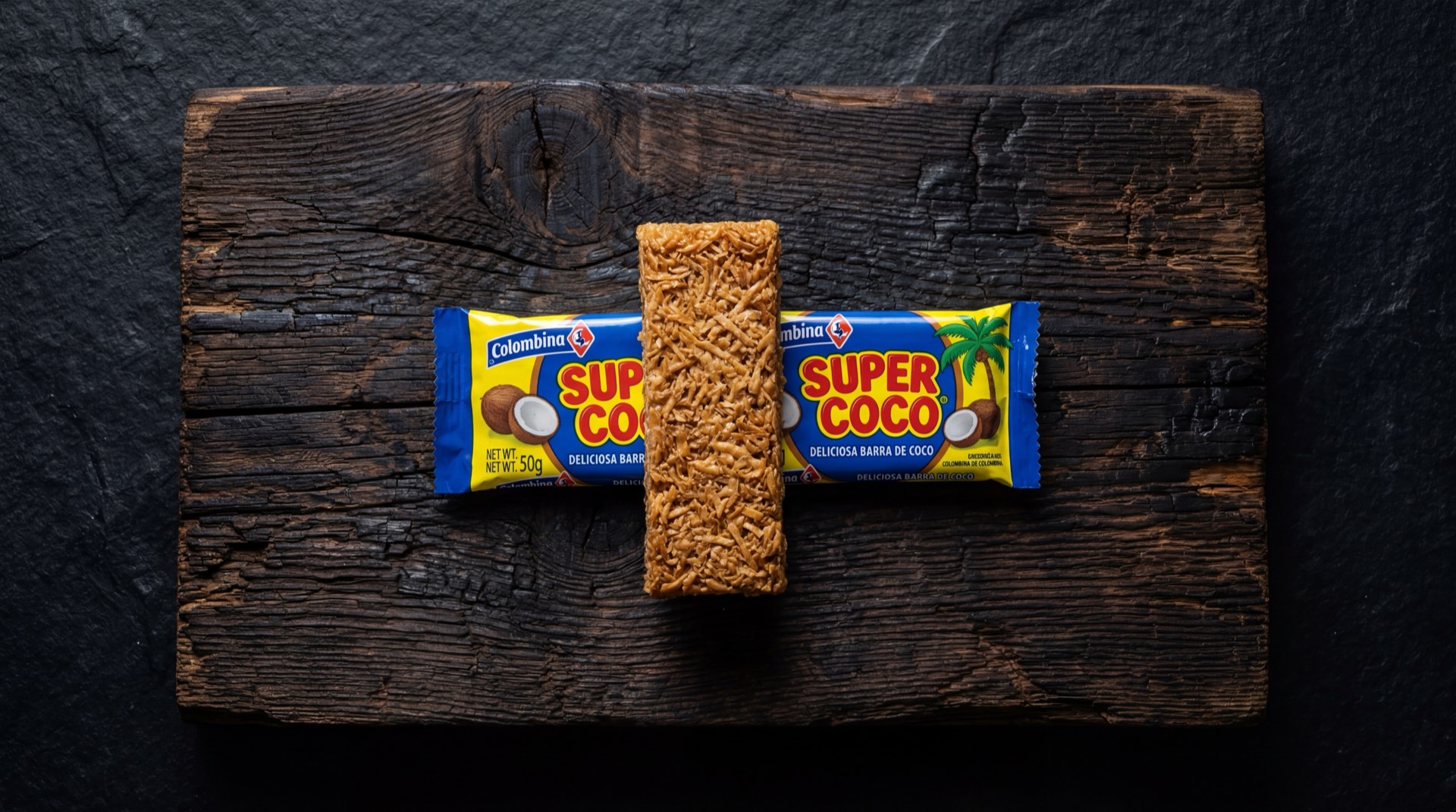 Super Coco de Colombina, barra de coco rallado dorada sobre plato de ceramica negra en mesa de marmol oscuro