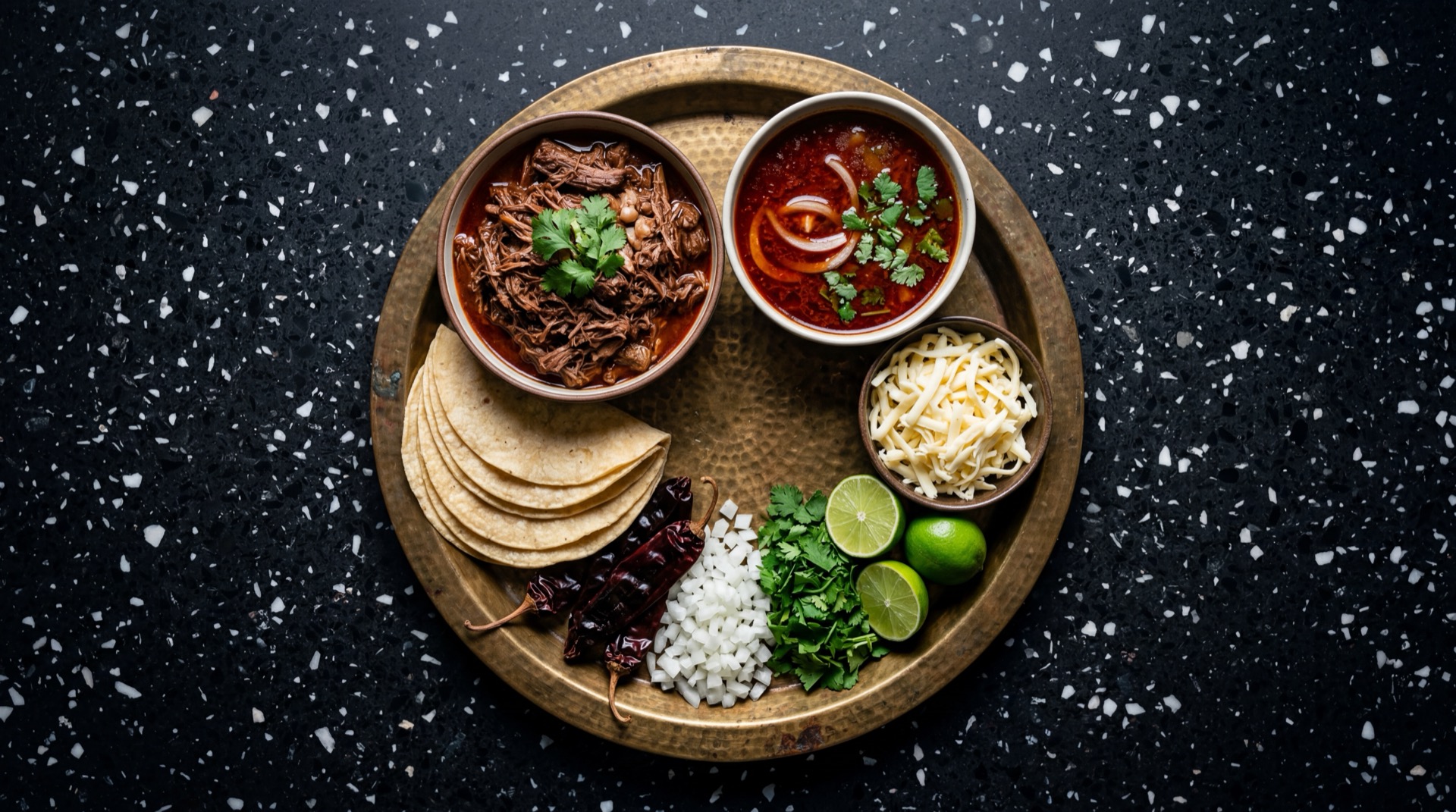 Ingredientes para tacos de birria de res: chamorro de res con hueso crudo, chiles guajillo secos, chiles ancho secos, chiles morita secos, tomates rojos maduros, ajo entero, cebolla blanca, oregano mexicano seco, comino molido, clavos de olor enteros, pimienta negra entera y tortillas de maiz frescas