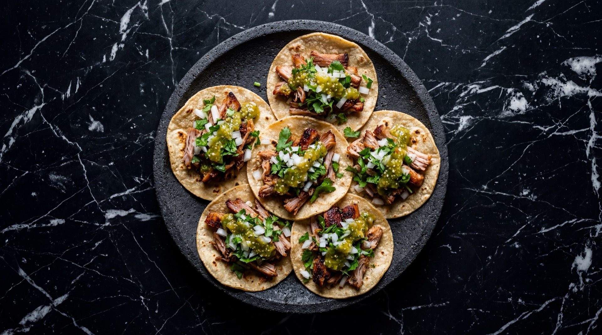 Tacos de carnitas michoacanas en tortillas de maiz con cilantro fresco picado, cebolla blanca y salsa verde en plato de barro sobre mesa de madera oscura