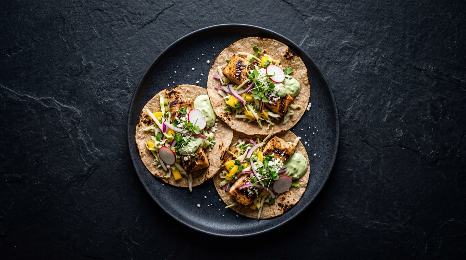 Tacos de pescado estilo Baja version saludable con filete de pescado blanco a la plancha sin capear, tortilla de maiz nixtamalizado, repollo morado rallado, pico de gallo fresco y limon verde sin crema de chipotle