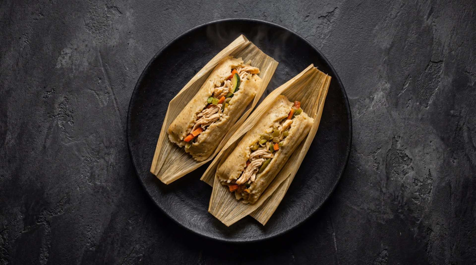 Tamales mexicanos version saludable con menos manteca de cerdo y relleno de pechuga de pollo deshebrada con verduras frescas sobre plato de basalto volcanico