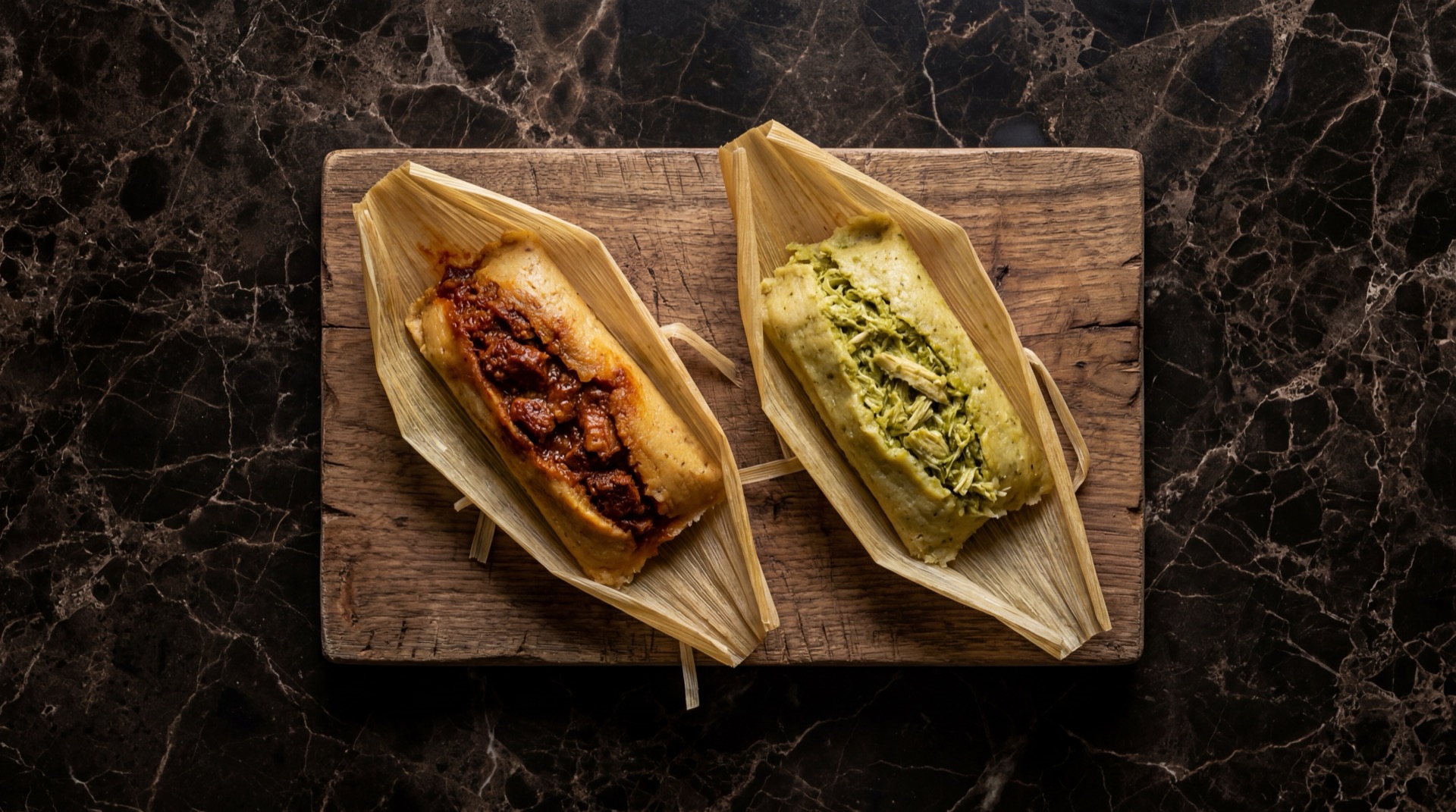 Tamales mexicanos abiertos en hojas de maiz secas remojadas mostrando la masa de maiz dorada y el relleno de pollo deshebrado en salsa verde sobre plato de ceramica negra mate