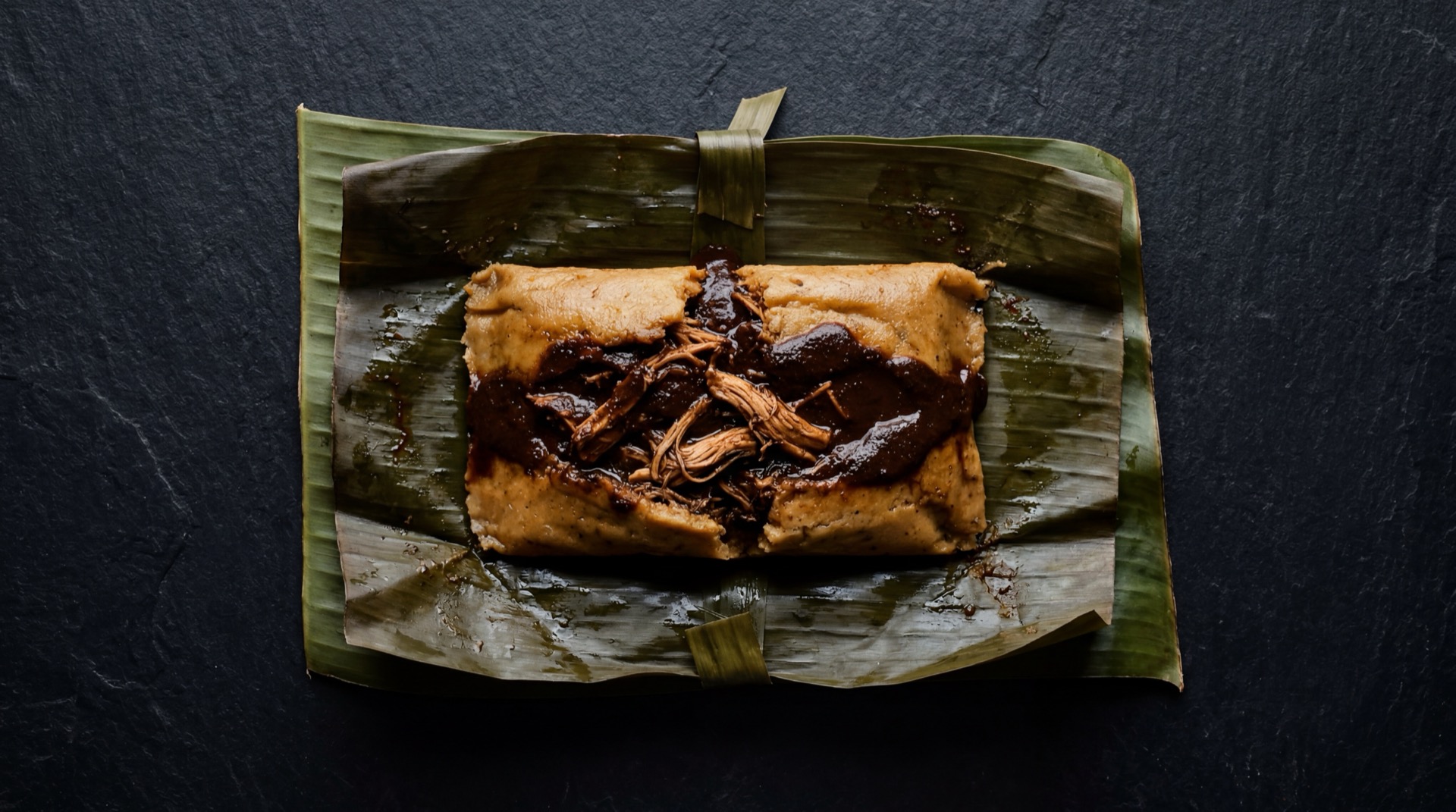Tamales Oaxaquenos mexicano tradicional servido en plato oscuro sobre mesa de marmol negro