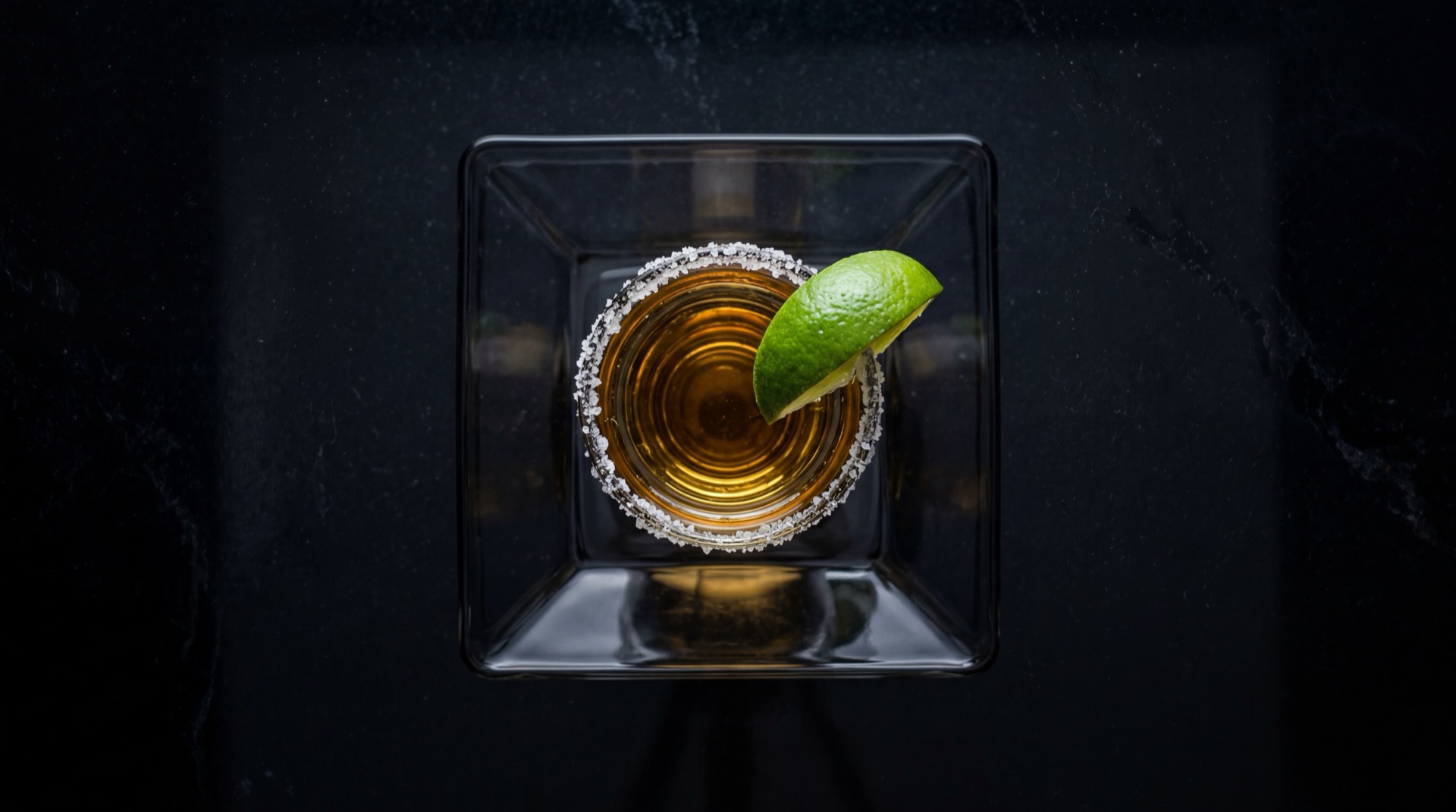 Tequila mexicano tradicional servido en plato oscuro sobre mesa de marmol negro