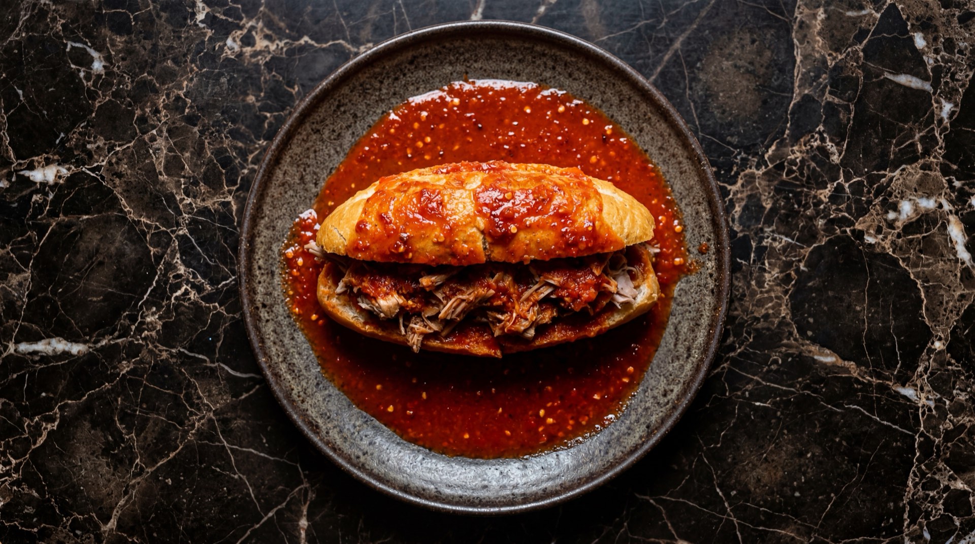 Torta ahogada de Guadalajara en birote salado rellena de carnitas de cerdo y banada en salsa de chile de arbol sobre plato de barro vidriado