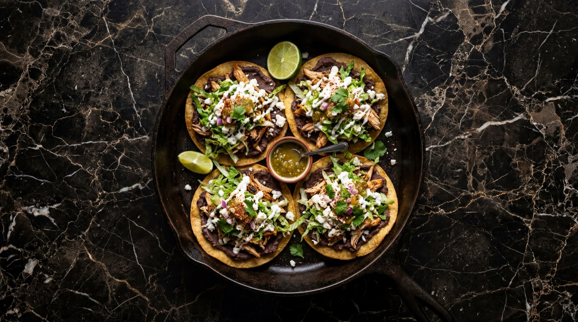 Tostadas mexicanas de tinga de pollo desmenuzado con lechuga iceberg, crema agria y queso fresco desmoronado sobre plato de obsidiana negra