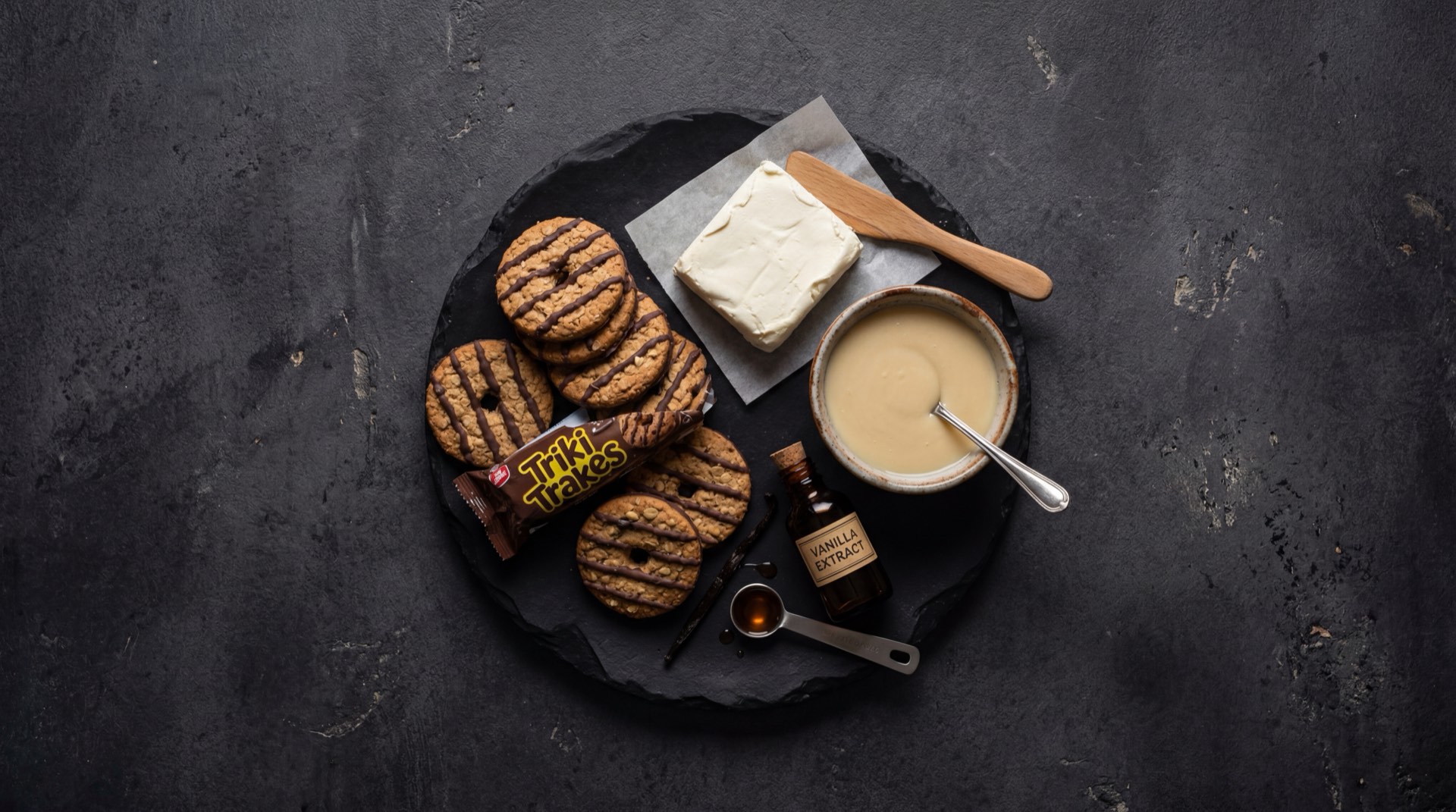 Galleta Triki Trakes abierta mostrando las dos tapas de galleta de chocolate oscuro y la crema de vainilla blanca del centro, con harina de trigo fortificada, cacao en polvo y azucar al lado
