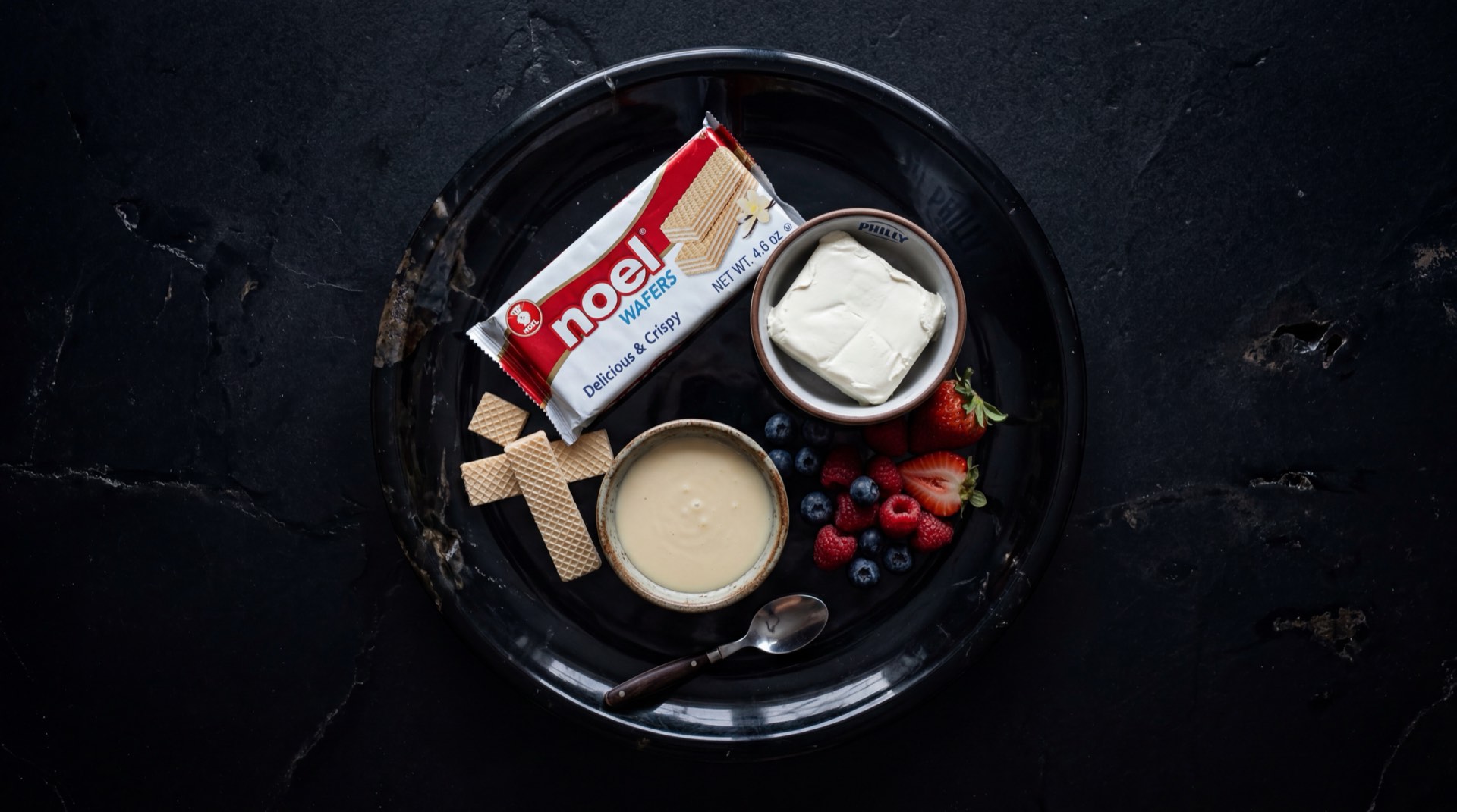 Wafer Noel abierto mostrando las capas de masa horneada de trigo y crema de vainilla, con harina de trigo refinada, azucar blanca y aceite vegetal al lado