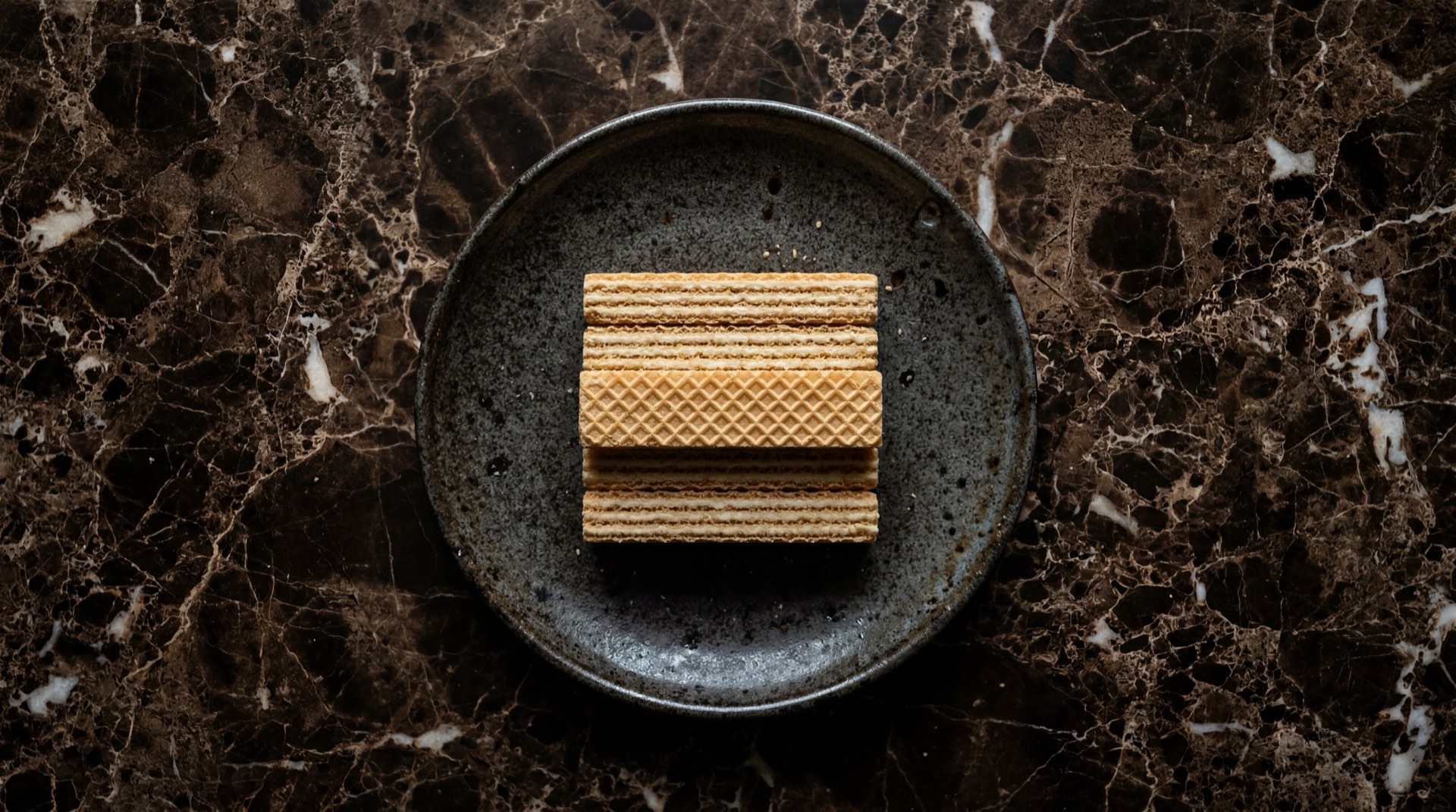 Wafer Noel de vainilla, galletas rectangulares con capas de crema sobre plato de basalto volcanico y mesa de marmol negro con vetas doradas