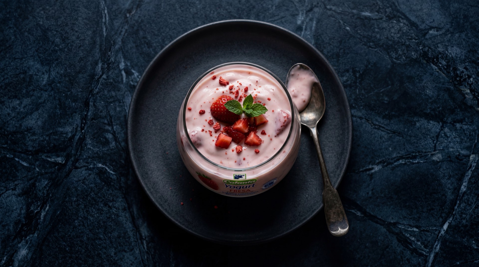 Yogurt Colanta de fresa en vaso plastico sobre mesa de marmol oscuro, yogur cremoso rosado de cooperativa lechera colombiana